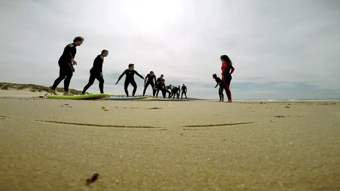 Uma fila de alunos a treinar o take off em cima das pranchas na areia, com o treinador a acompanhar