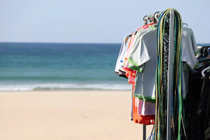 Licras e fatos pendurados num bengaleiro na praia, com o mar em fundo