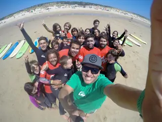Treinadores e crianças juntos na areia a seguir a uma aula, com as pranchas alinhadas atrás